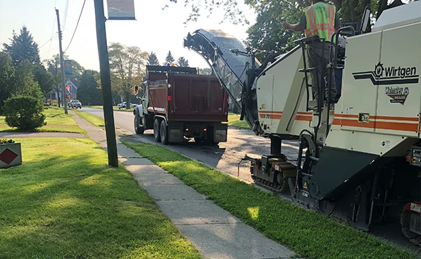 A Peters Paving dump truck collecting asphalt debris from a Wirtgen cold planer during a residential street milling project.