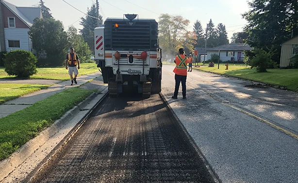 A Peters Paving Wirtgen milling machine performing precision pavement removal along a concrete curb line for road restoration.