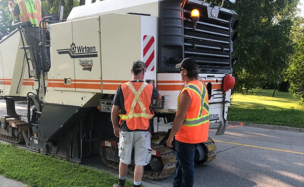 A Wirtgen milling machine on a residential street with workers.