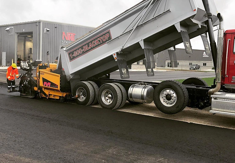 Peters Paving industrial asphalt crew using a Mauldin paver and 1-800-BLACKTOP dump truck for a large-scale commercial project.