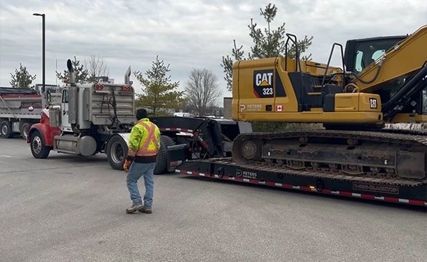 A Peters Paving transport truck and specialized lowboy trailer floating a CAT 323 excavator to a new project site.