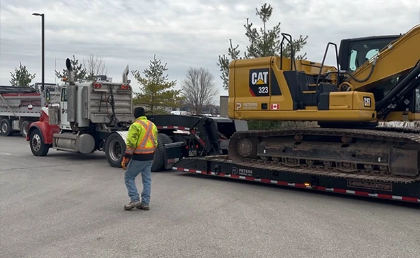 Peters Paving branded CAT 323 excavator being mobilized on a lowboy trailer for a large-scale earthmoving and excavation project.