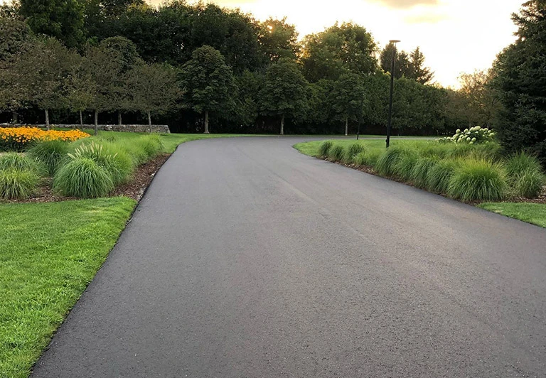 Smoothly curved asphalt driveway integrated with professional garden landscaping and ornamental grasses.