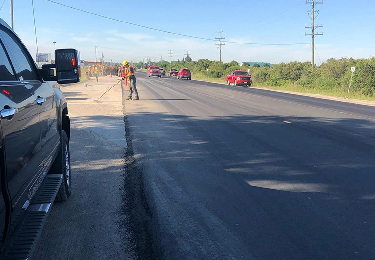 Peters Paving crew member performing manual site prep and asphalt edging for a multi-lane municipal road project.
