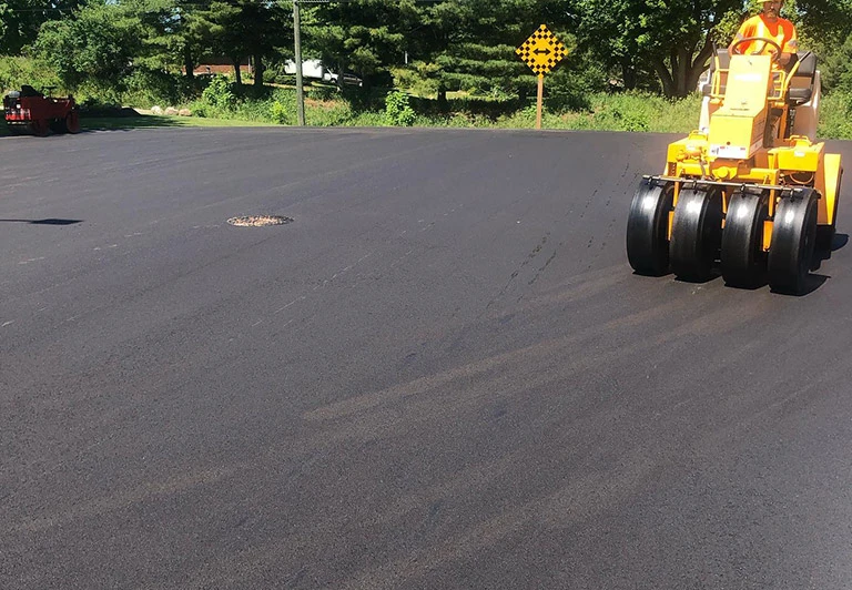 A Peters Paving pneumatic rubber-tire roller finishing a large asphalt surface for maximum durability and a smooth seal.