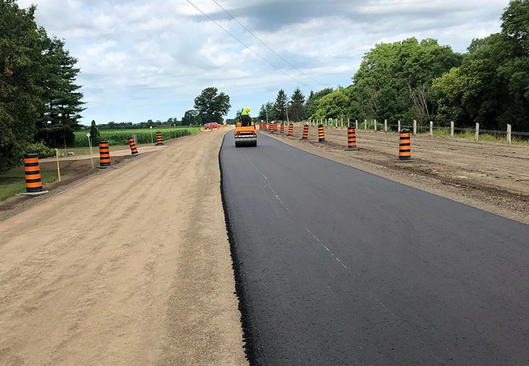 Peters Paving heavy-duty asphalt roller compacting a newly laid rural highway surface with safety pylons in place.