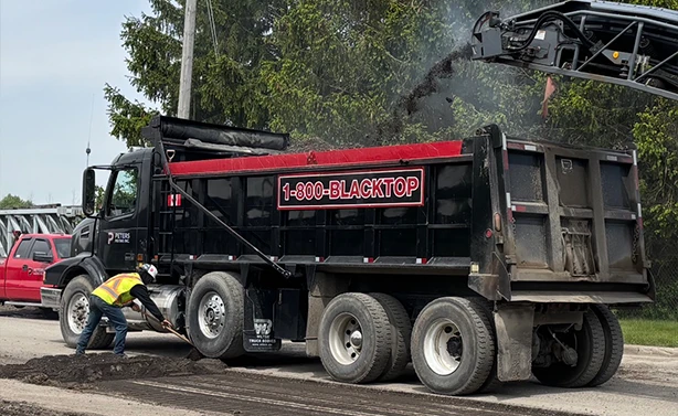 A Peters Paving 1-800-BLACKTOP dump truck receiving asphalt millings from a cold planer during a road reconstruction project.