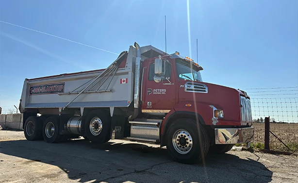 A Peters Paving Western Star dump truck with 1-800-BLACKTOP branding parked at a rural job site under a clear blue sky.